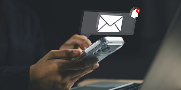 Close-up image of a hand holding a phone with a large "notification" popping out of it with an envelope icon inside. Beside it is a smaller notification bell icon.
